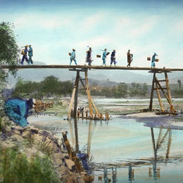 Photograph of farmers crossing a river on a wooden bridge